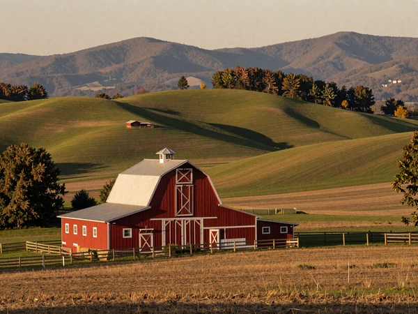 North Carolina Piedmont farmland with a red tobacco barn, green rolling hills, and the Blue Ridge Mountains in the distance